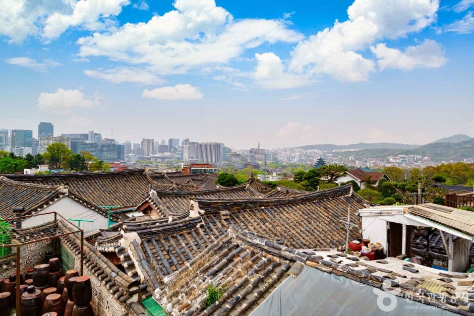 Rows of curved grey hanok roof tiles descending a hillside toward the Seoul skyline