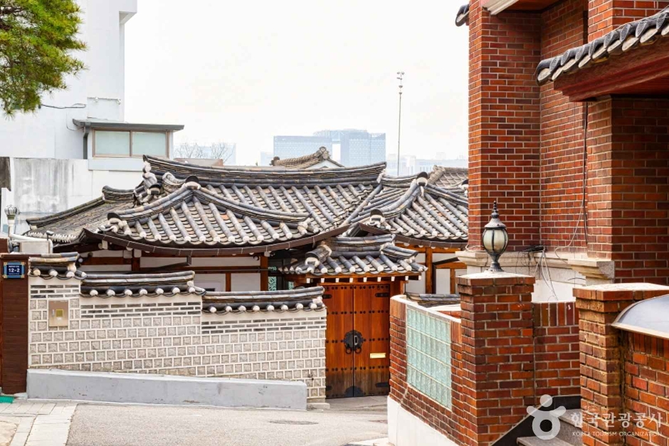 A hanok gate with a lamp beside a brick pillar at a quiet corner of the neighbourhood