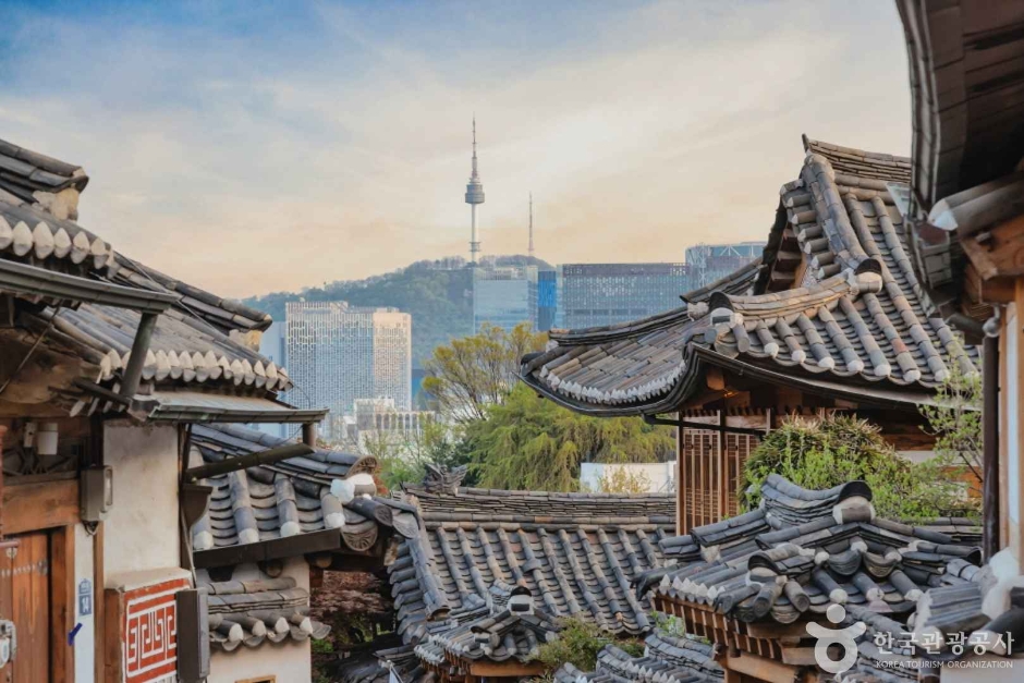 Layered hanok roofs in low golden light with N Seoul Tower on the skyline behind