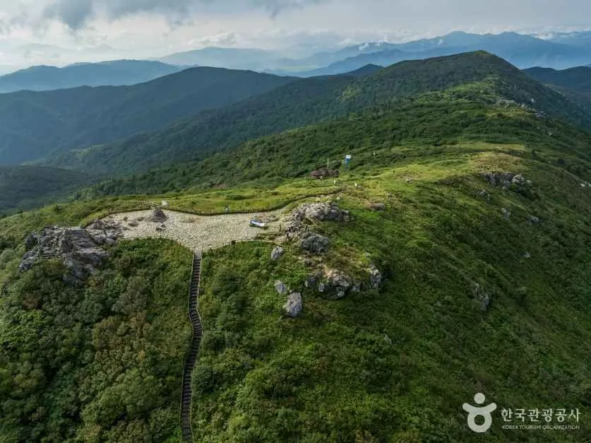 A green mountain ridge with a footpath running along it under a bright summer sky