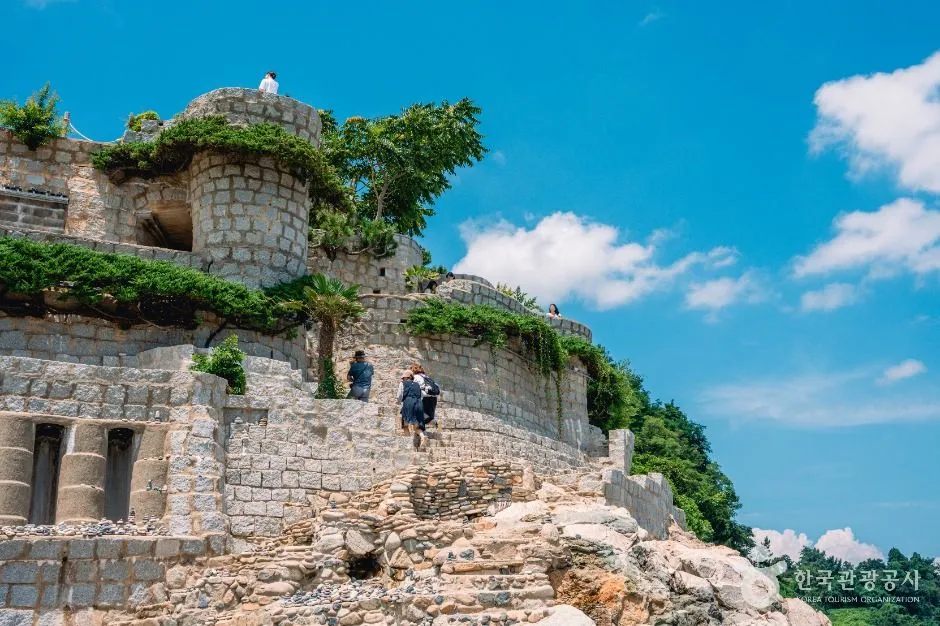 Stone walls and arches of the hand-built castle rising against a bright sky, with a visitor for scale