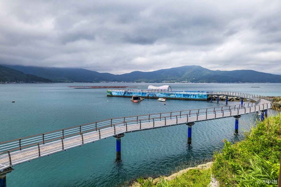 A long low footbridge running out over calm sea water toward a small pier