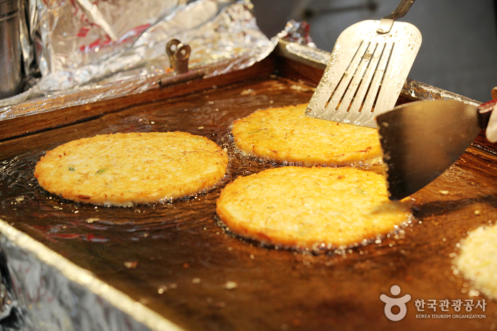 広蔵市場の平たい鉄板で、緑豆のチヂミ（ピンデトク）が油の中で焼かれている