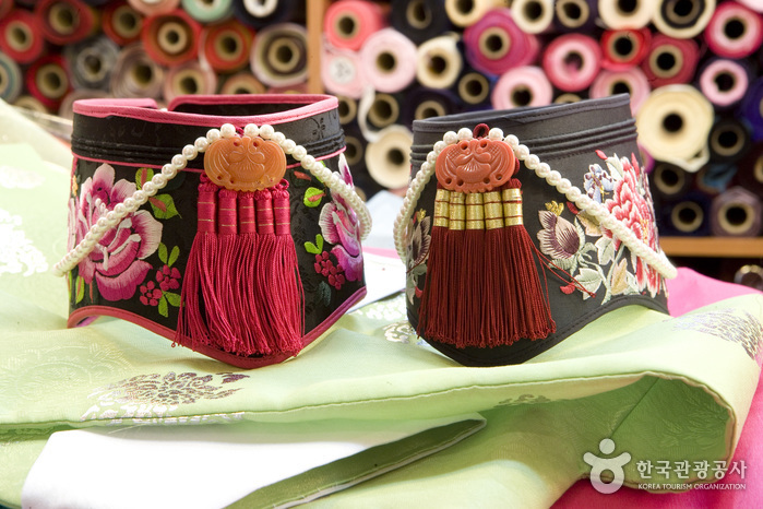 Traditional Korean embroidered headpieces displayed in front of rolls of patterned fabric