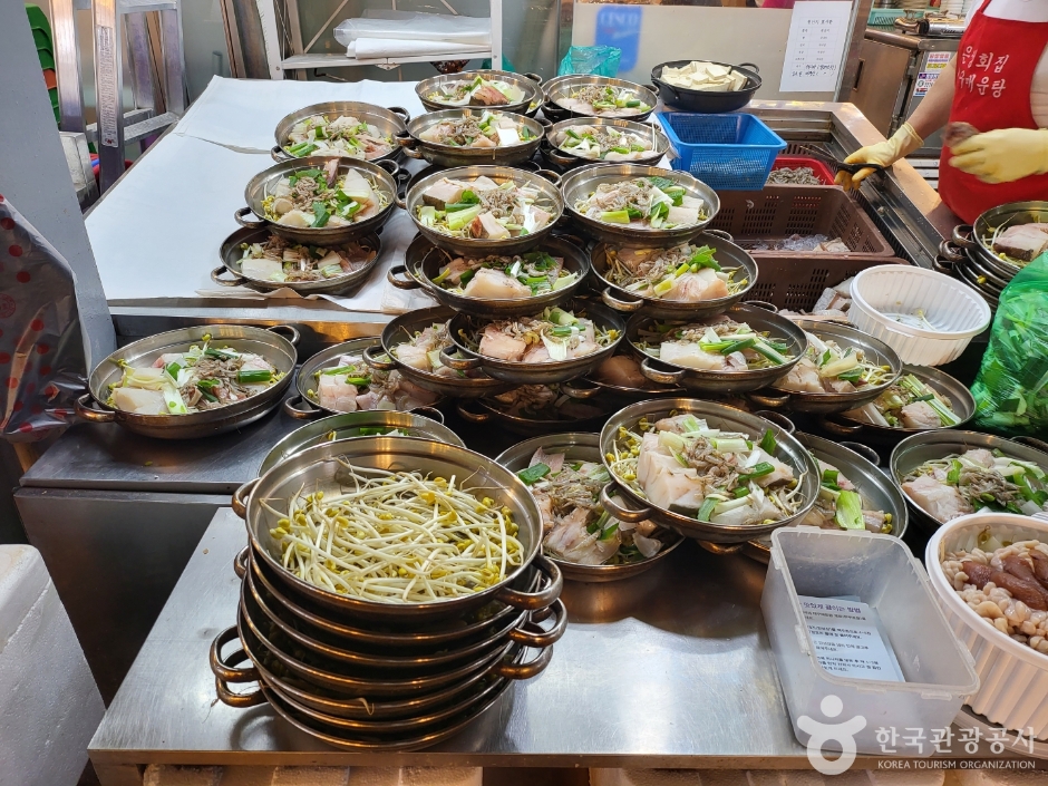 Rows of prepared bibimbap bowls and side dishes lined up on a stainless counter at a Korean market stall