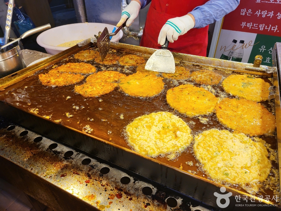 Golden mung-bean pancakes frying in oil on a large flat griddle at a market stall