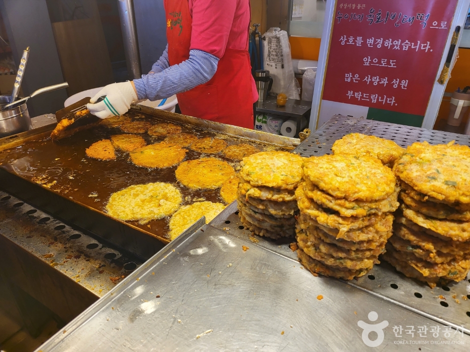 市場の屋台で、焼き上がった緑豆チヂミが鉄板の脇に高く積み上げられている