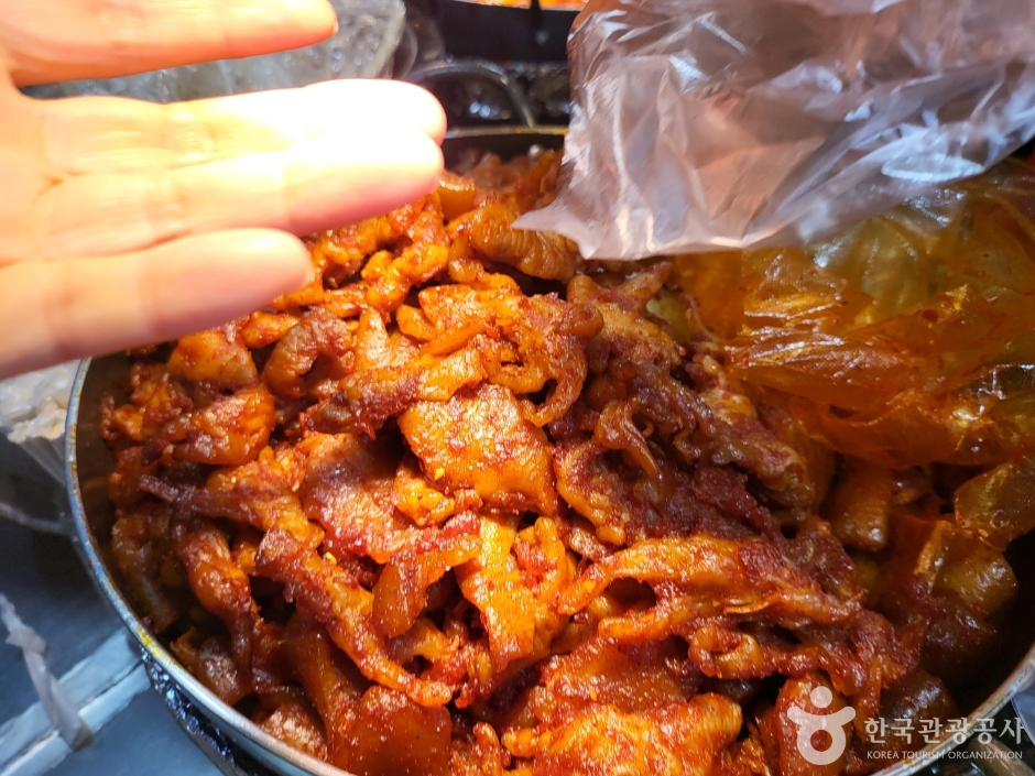 A hand serving a bowl of red, spicy stir-fried food at a market stall