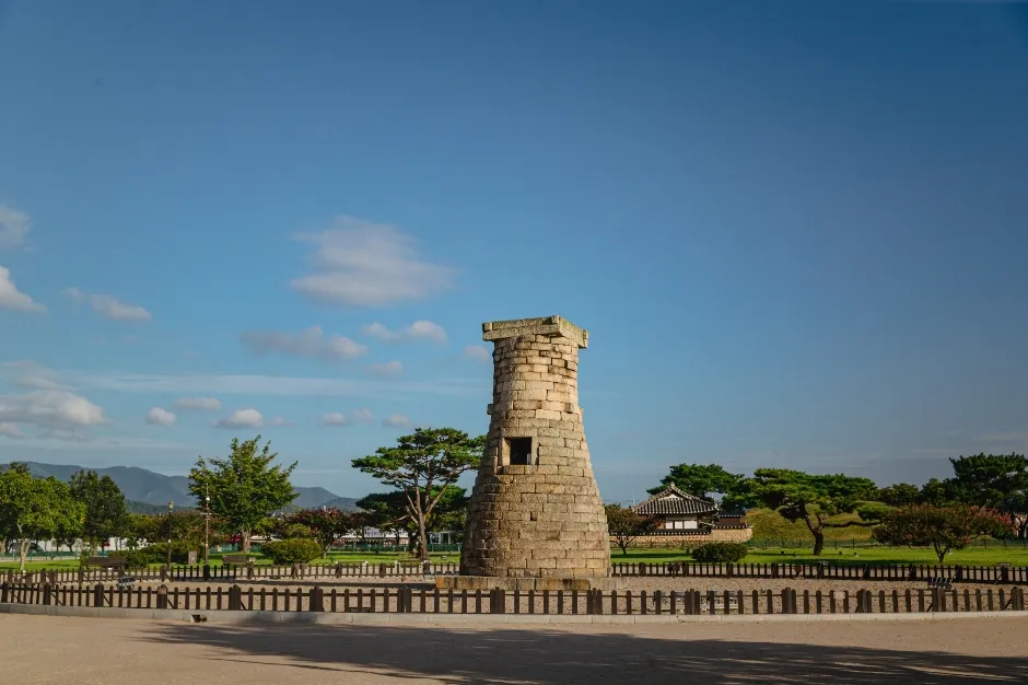 The stone tower of Cheomseongdae standing alone in an open grass field with low hills behind