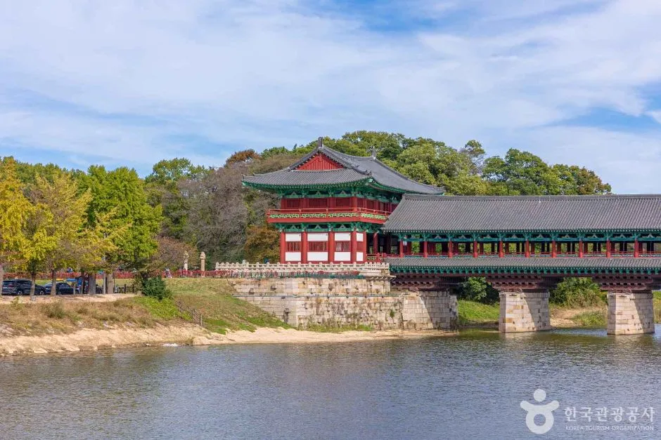 Woljeonggyo bridge seen in daylight from the riverbank, a long wooden roofed structure spanning the water