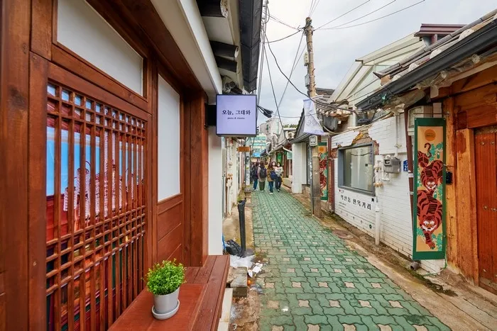 A small square sign reading 오늘, 그대와 hanging from a hanok eave beside a wooden lattice door in Ikseondong