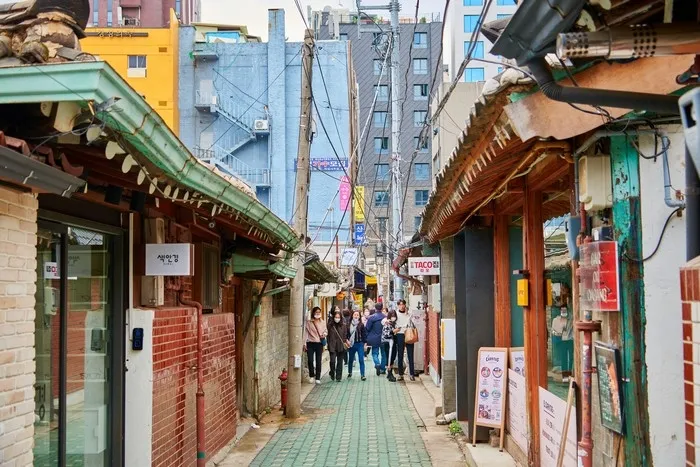 益善洞の狭い韓屋の路地。縦書きのハングル看板と立て看板のメニューが並び、瓦屋根の間を人が歩いている
