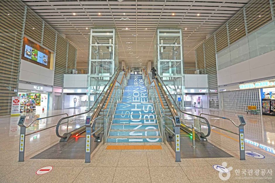 仁川国際空港第2ターミナルの館内、上りエスカレーターの両側に案内表示と店舗が並ぶ