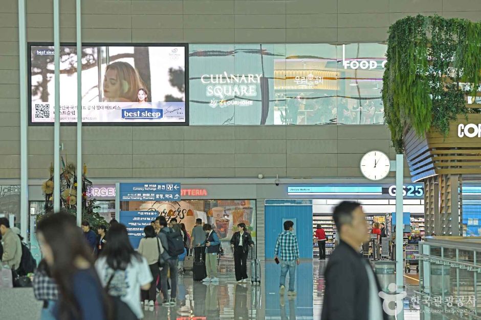 Travellers walking through a concourse at Incheon Airport past a bank of information screens and shop signs