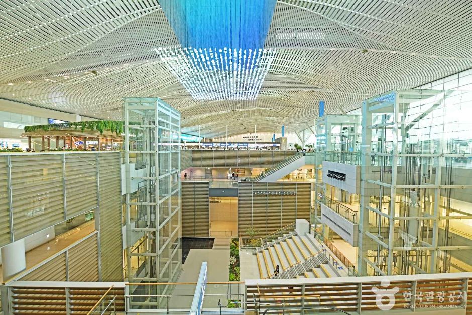 The bright glass-roofed transport centre atrium at Incheon International Airport with escalators leading down