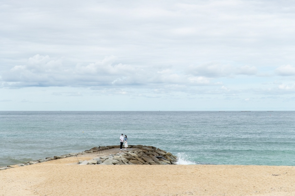 Two people standing at the end of a rocky breakwater running out from the beach into the East Sea at Jumunjin