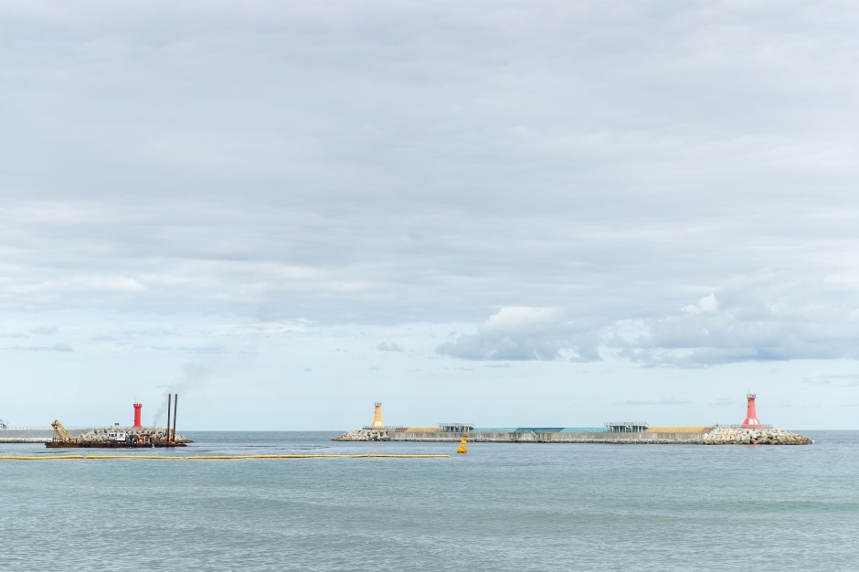 The outer breakwaters at Jumunjin with red and orange lighthouses, seen from shore