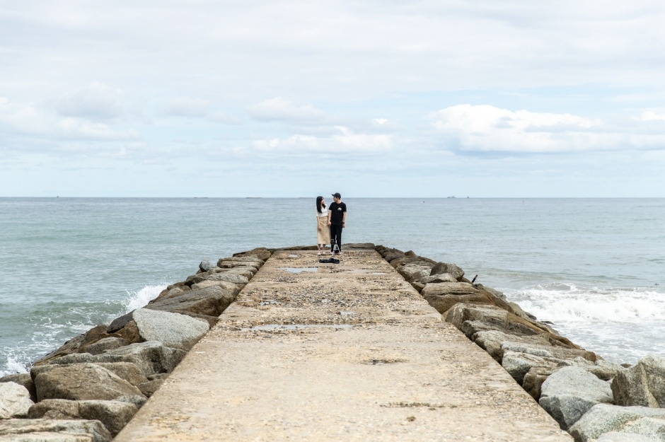 Two people standing close together at the far end of a concrete breakwater with open sea beyond