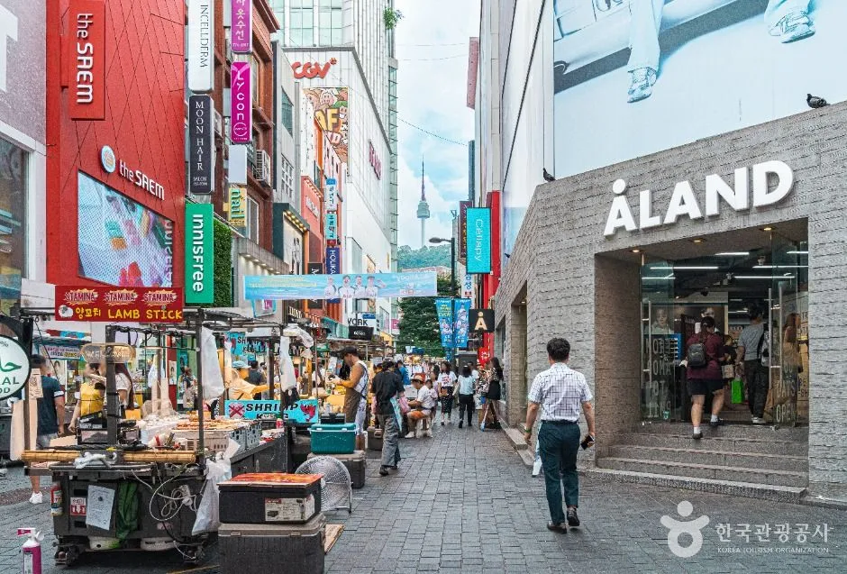 明洞の歩行者通り、両側に店が並び、中央には屋台、背後の丘にNソウルタワー