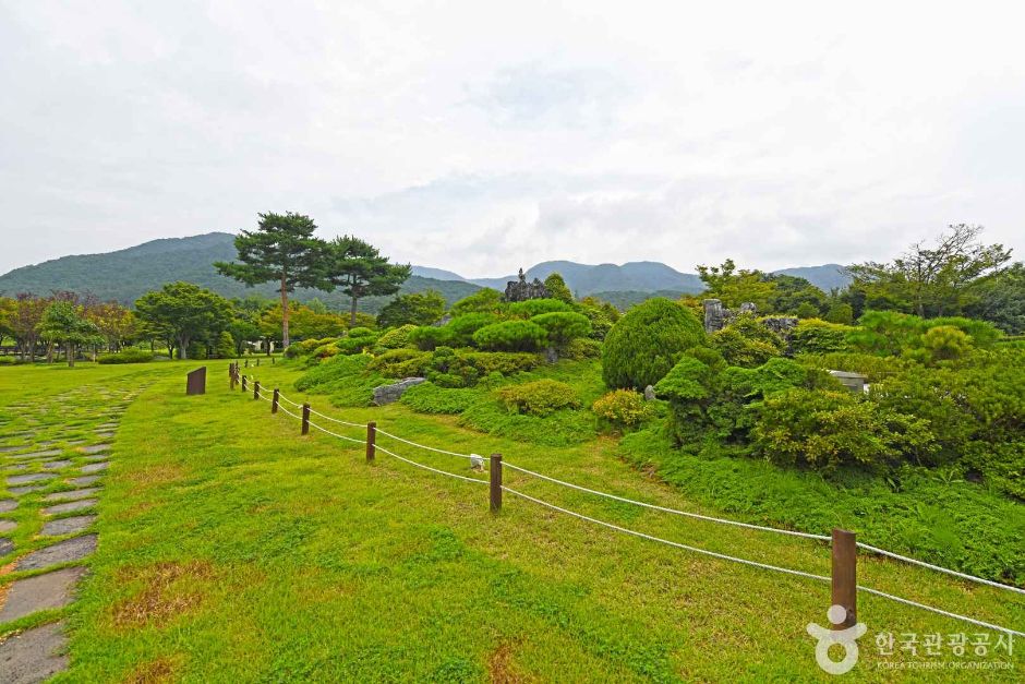 A wide lawn with clipped shrubs and low hills behind, all in summer green
