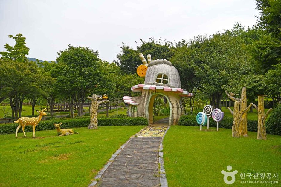 Whimsical outdoor sculptures including a mushroom house and a deer beside a paved garden path