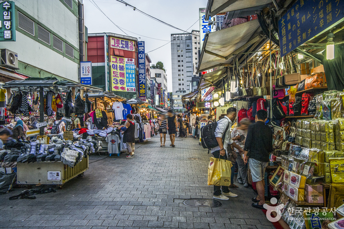 A crowded lane of stalls and shopfronts running between tall buildings at Namdaemun Market