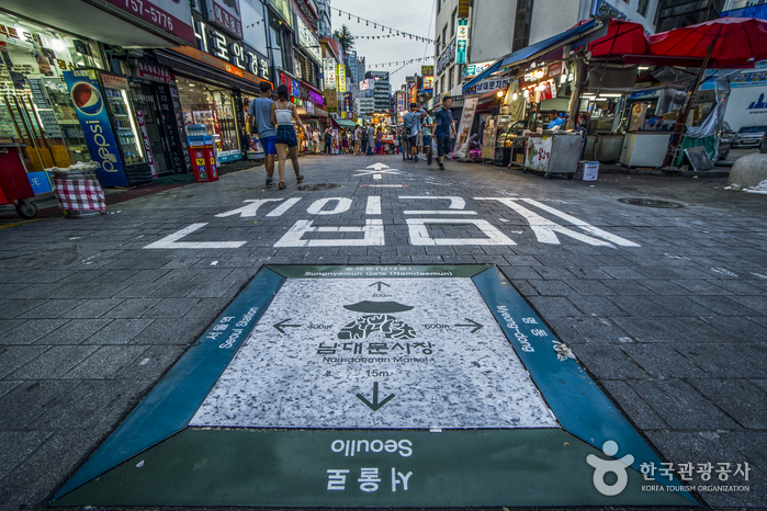 A pedestrian lane in Namdaemun Market painted with a no-vehicle marking and a direction sign to Seoul Station