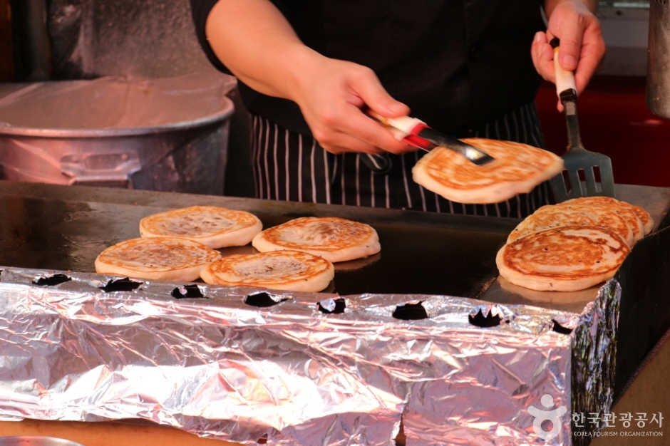 A vendor pressing hotteok flat on a griddle with a metal turner