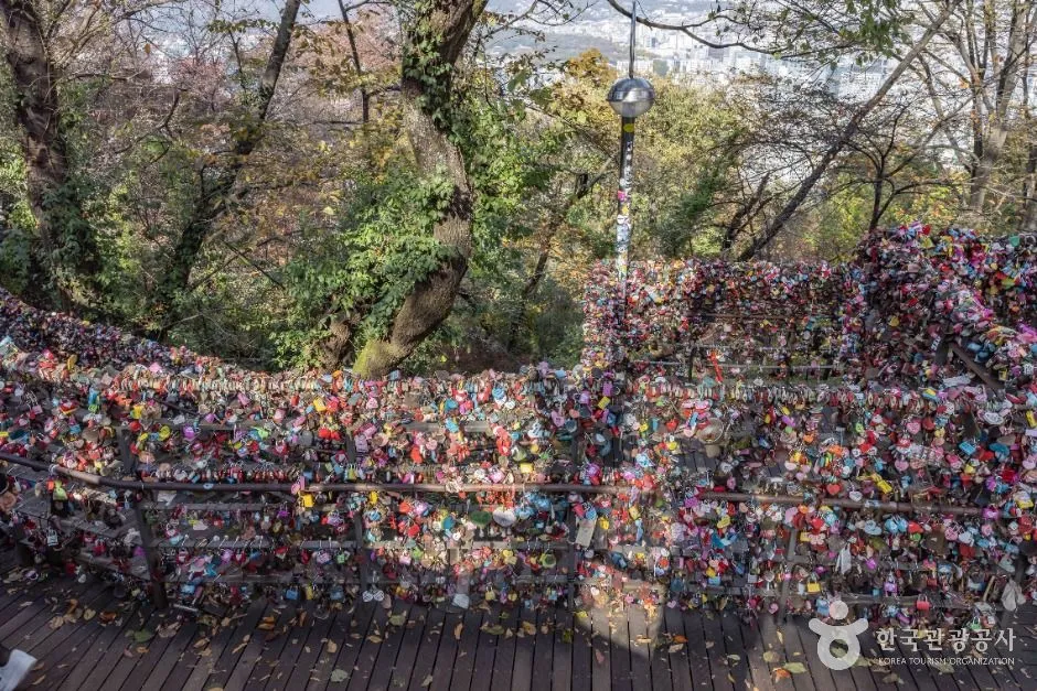 A dense wall of padlocks in many colours fastened to railings, with bare trees behind