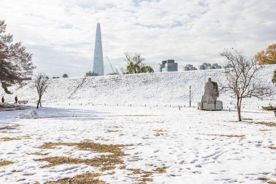 雪に覆われたオリンピック公園の広い芝地、手前に彫刻、遠景の空にロッテワールドタワー