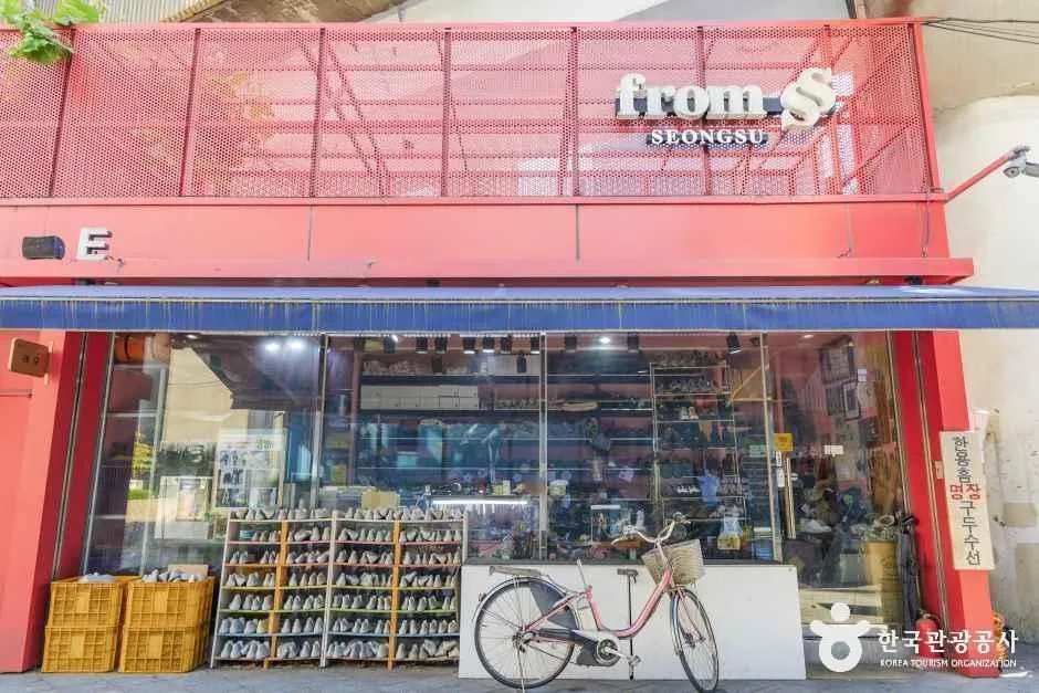 A shopfront framed in a red steel container structure signed from SS SEONGSU, with shelves of shoes inside and a bicycle parked at the kerb